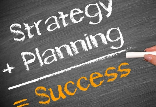 על הלוח כתוב בגיר: אסטרטגיה פלוס תכנון שווה הצלחה, מצביע על תרומתו של יועץ עסקי בבניית אסטרטגיה לעסק